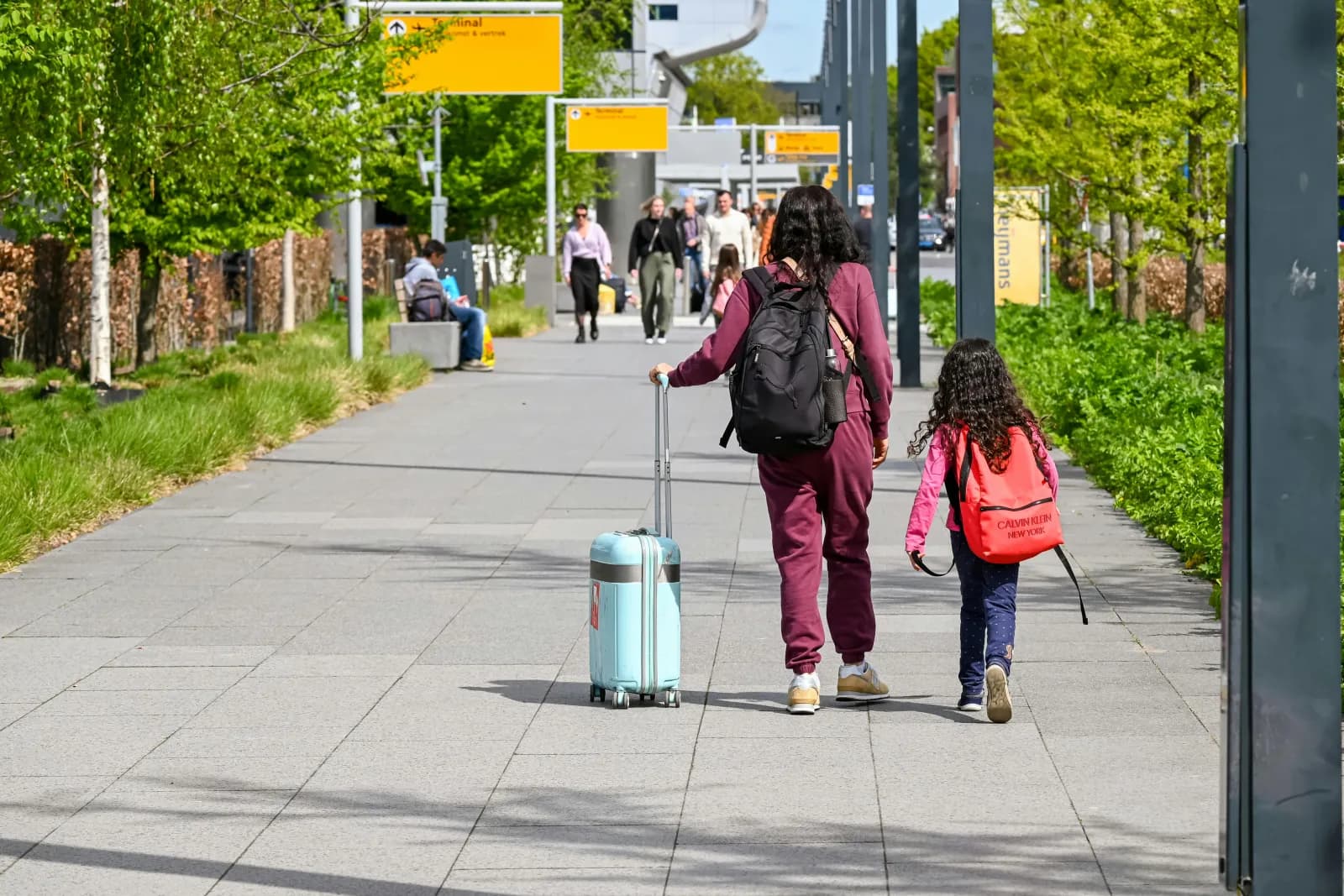 Mor og datter med bagasje utendørs i sollys, klare for avreise