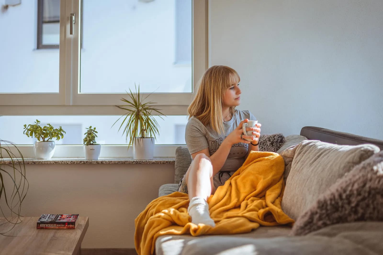 Kvinne sitter i en sofa med en kaffekopp i et rolig vindueslys, omgitt av planter
