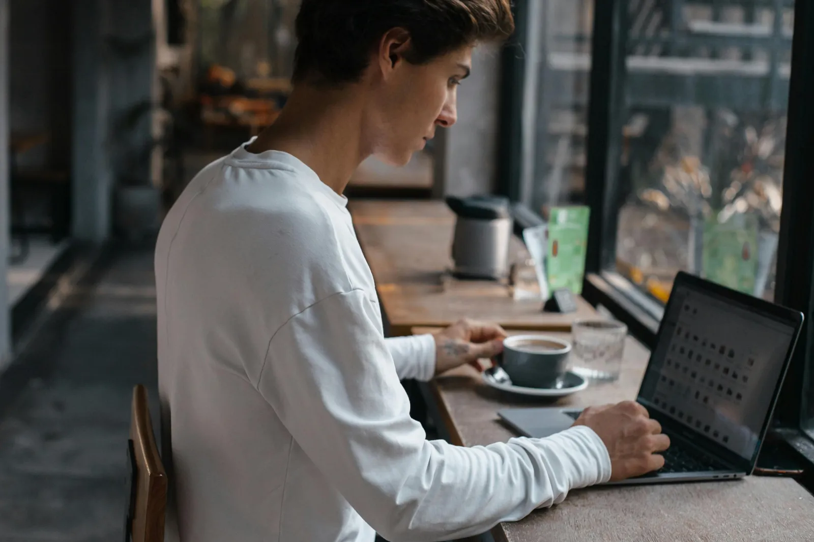 Mann konsentrert ved skrivebordet med laptop og kaffe, fordypet i dokumenter