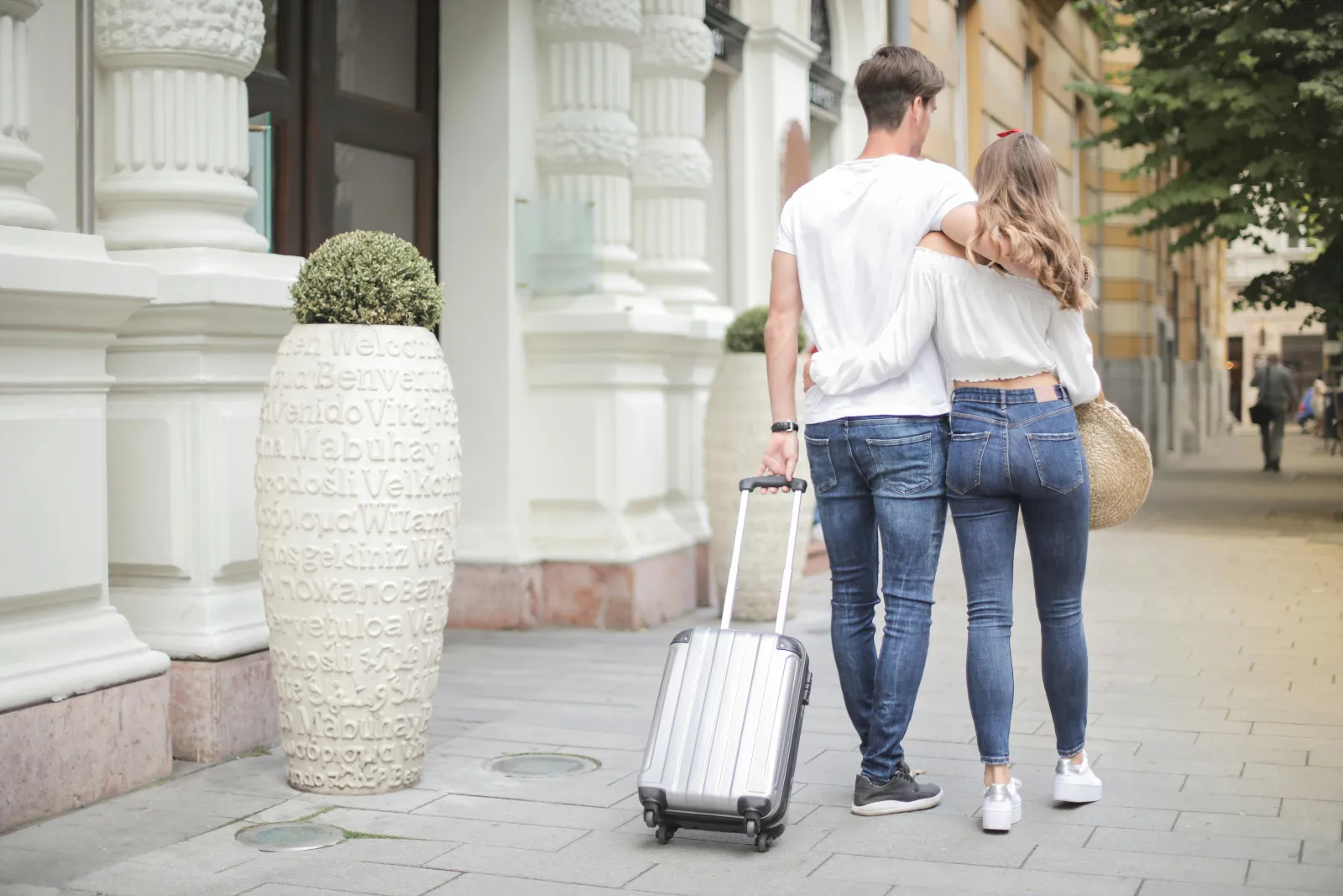 Par med koffert i en solfylt bygate, klem og glad stemning på vei mot reisen